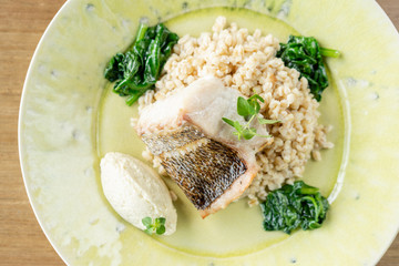Roasted pike perch or cod fish with bulgur. Dish decorated with a spinach. Restaurant menu