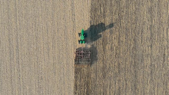 Top-Down Tracking Drone Shot Above a Green Tractor Plowing a Field on a Sunny day.
