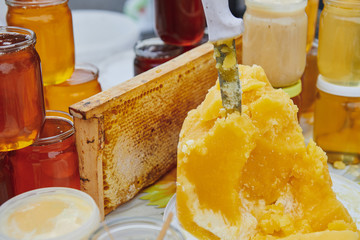 A lot of honey products at the market. Jars with different varieties of honey. The knife sticks out...