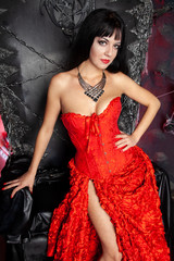 beautiful vampire woman in red long dress near big black throne in the studio