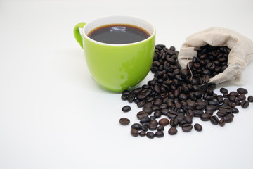 Black coffee in a green mug and coffee beans in the sack and outside of the sack resting