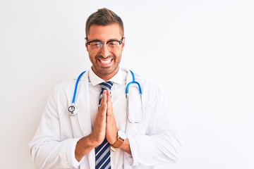 Fototapeta premium Young handsome doctor man wearing stethoscope over isolated background praying with hands together asking for forgiveness smiling confident.