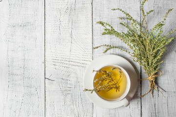 White cup of healthy herbal thyme tea with fresh thyme leaves bunch on white wooden rustic...