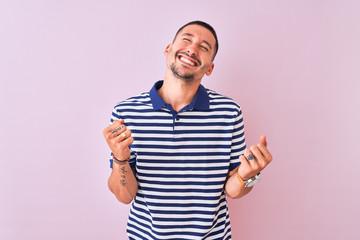 Young handsome man wearing nautical striped t-shirt over pink isolated background very happy and excited doing winner gesture with arms raised, smiling and screaming for success. Celebration concept.