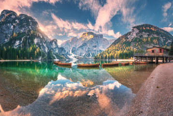 Amazing Braies lake at sunrise in autumn in Dolomites, Italy. Landscape with mountains, sky with clouds, boats, water with reflection, trees with colorful leaves. Lake in fall. Italian alps. Panorama - obrazy, fototapety, plakaty