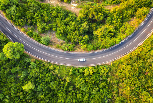 Aerial view of road with car in beautiful forest at sunset in summer. Colorful landscape with asphalt road, trees with green leaves. Highway through the park. Top view. Natural colors.  Nature