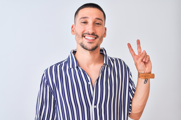 Naklejka premium Young handsome man wearing nautical striped shirt standing over isolated background smiling with happy face winking at the camera doing victory sign. Number two.