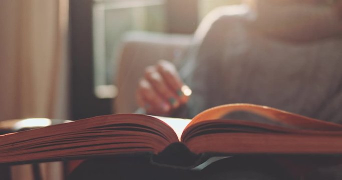 Woman's Hand Turning Pages of a Book, Cozy Morning. SLOW MOTION, CLOSE UP. Unrecognizable Girl reading a book and holding fingers along the lines. Cinematic light, comfort of a home. Lens Flare.
