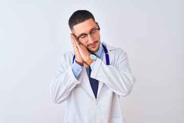 Young doctor man wearing stethoscope over isolated background sleeping tired dreaming and posing with hands together while smiling with closed eyes.