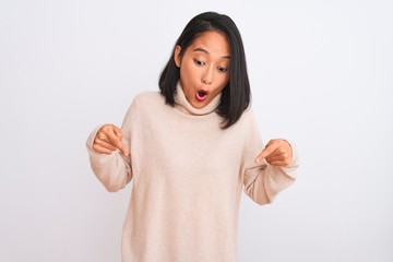 Young chinese woman wearing turtleneck sweater standing over isolated white background Pointing down with fingers showing advertisement, surprised face and open mouth © Krakenimages.com