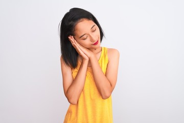 Young chinese woman wearing yellow casual t-shirt standing over isolated white background sleeping tired dreaming and posing with hands together while smiling with closed eyes.