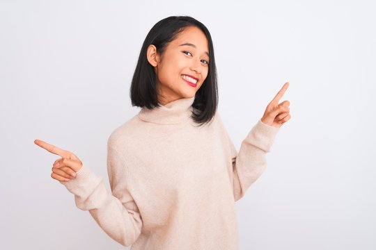 Young chinese woman wearing turtleneck sweater standing over isolated white background smiling confident pointing with fingers to different directions. Copy space for advertisement