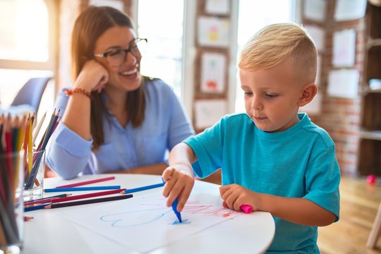 Young caucasian child playing at playschool with teacher. Mother and son at playroom drawing a draw with color pencils