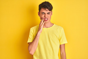 Teenager boy wearing yellow t-shirt over isolated background touching mouth with hand with painful expression because of toothache or dental illness on teeth. Dentist concept.