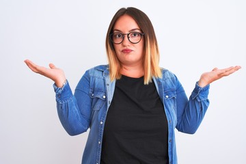 Young beautiful woman wearing denim shirt and glasses over isolated white background clueless and...
