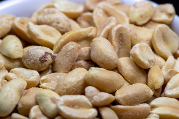 macro photography of shelled and salted peanuts in a white canister with black background
