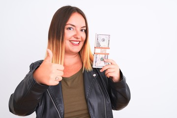 Young beautiful woman holding dollars standing over isolated white background happy with big smile doing ok sign, thumb up with fingers, excellent sign