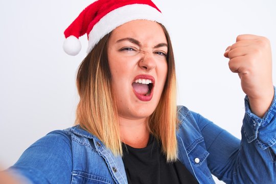 Beautiful woman wearing Christmas Santa hat make selfie over isolated white background annoyed and frustrated shouting with anger, crazy and yelling with raised hand, anger concept