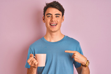 Teenager boy drinking a cup of coffee over isolated pink background very happy pointing with hand and finger