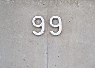Number 99, ninety-nine, metallic digits on gray concrete background.