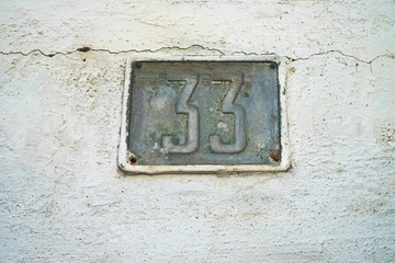 Number 33, thirty-three, old house number plate on a weathered wall background.