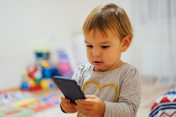 Baby using phone, playing game or watching cartoons. Home indoors. Screen time