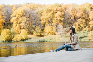 Naklejka na ściany i meble A young girl sketching near a lake in the autumn forest.