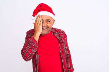 Middle age man wearing Christmas Santa hat standing over isolated white background covering one eye with hand, confident smile on face and surprise emotion.
