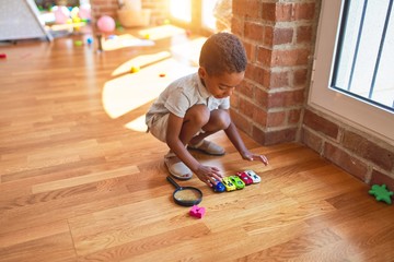 Beautiful african american toddler playing with cars around lots of toys at kindergarten