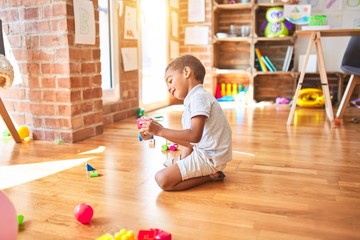 Beautiful african american toddler playing with wooden blocks train toy around lots of toys at kindergarten