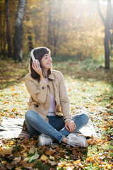 Young girl listening to music with headphones in the autumn forest. The girl is in a great mood and happy