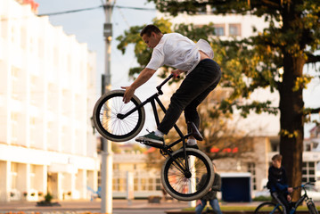 The guy performs a stunt on BMX, jumping up, and touches the front wheel.