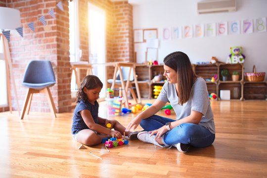 Beautiful teacher and toddler girl playing with train at kindergarten