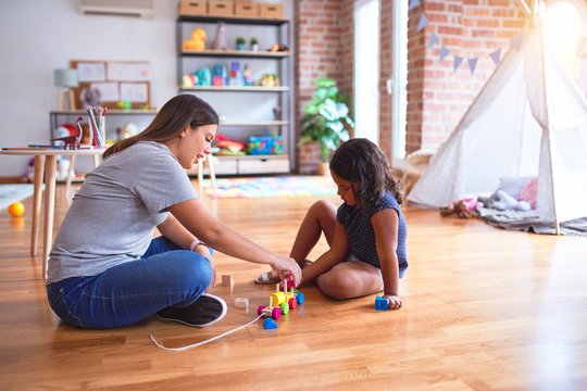 Beautiful teacher and toddler girl playing with train at kindergarten