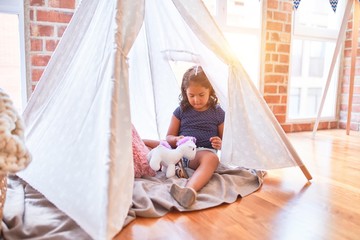 Beautiful toddler girl sitting on the floor playing with unicorn inside tipi at kindergarten © Krakenimages.com