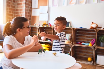 Beautiful teacher and toddler boy playing with figurine army soldiers at kindergarten