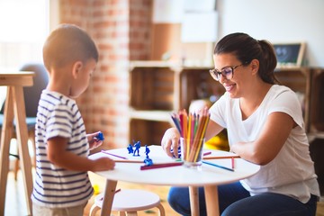 Beautiful teacher and toddler boy playing with figurine army soldiers at kindergarten