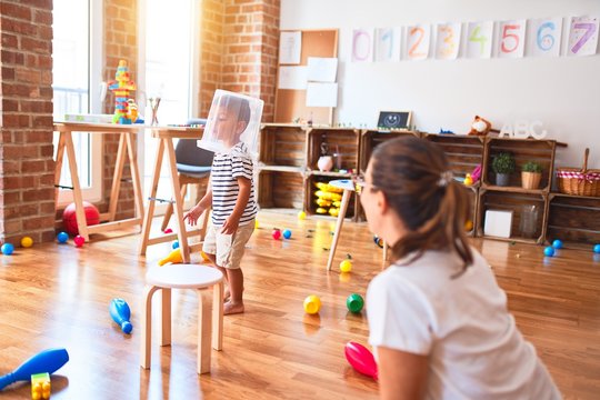 Beautiful teacher and toddler boy playing with plastic basket at kindergarten