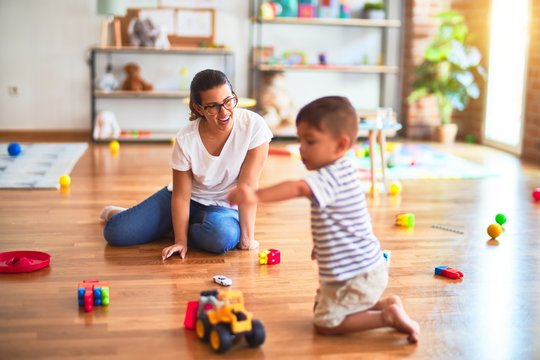 Beautiful teacher and toddler boy playing with tractor and cars at kindergarten