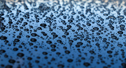 Drops of rain water on a glass surface reflecting various shades of blue and gray in an evening sky.