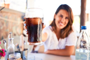 Young beautiful woman sitting at restaurant enjoying summer vacation drinking soda