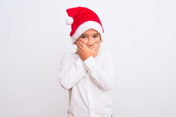 Beautiful kid boy wearing Christmas Santa hat standing over isolated white background shocked covering mouth with hands for mistake. Secret concept.