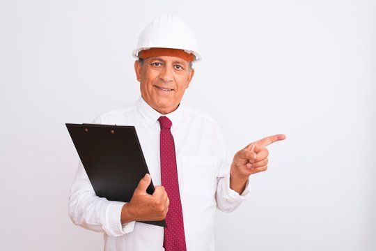 Senior architect man wearing security helmet holding clipboard over isolated white background very happy pointing with hand and finger to the side