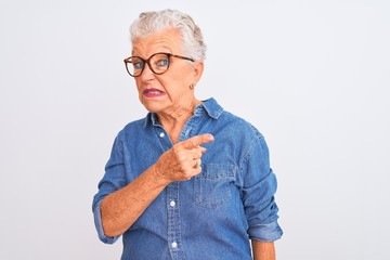 Senior grey-haired woman wearing denim shirt and glasses over isolated white background Pointing aside worried and nervous with forefinger, concerned and surprised expression