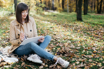 A young girl sketching near a lake in the autumn forest. Sketching. The girl is in a great mood and...