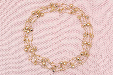 Obraz premium Circle frame from golden beads garland on knitted pink background. Top view Flat lay Template for design