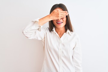 Young beautiful businesswoman wearing glasses standing over isolated white background smiling and laughing with hand on face covering eyes for surprise. Blind concept.