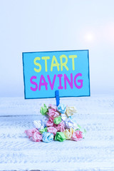 Text sign showing Start Saving. Business photo showcasing money that a demonstrating keeps in an account in a bank or like Reminder pile colored crumpled paper clothespin reminder white wooden space
