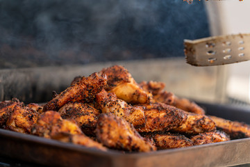 chicken wings piled up on a serving tray next to a smoker