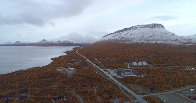 Kilpisjarvi village, Aerial, descending, drone shot, overlooking the town, the e8 road and first snow on Saanatunturi fell mountain, on a cold, autumn morning, in Enontekio, Finland